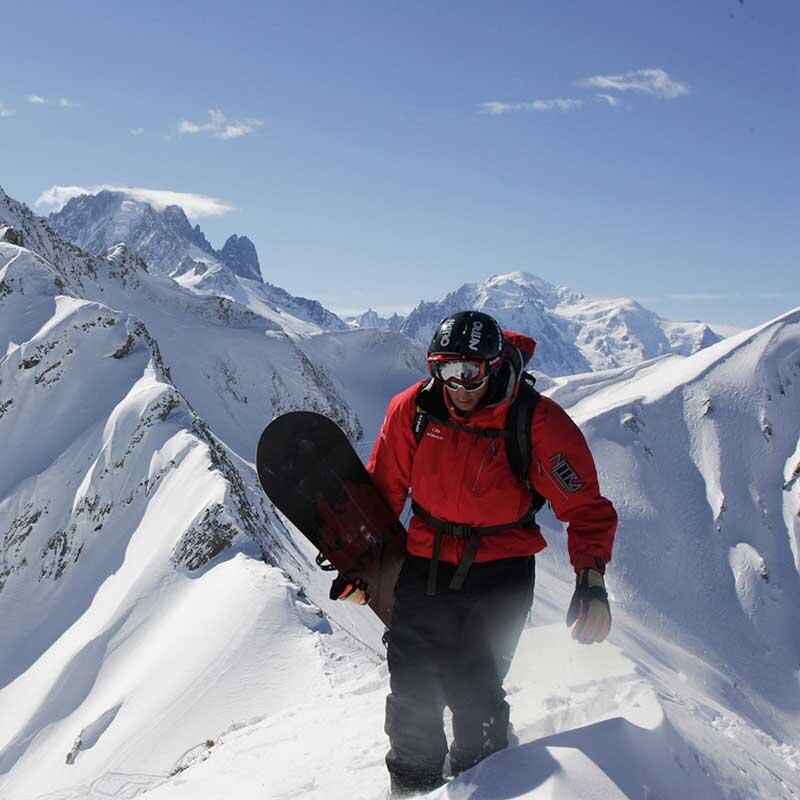 Person carrying their snowboard on top of a mountain